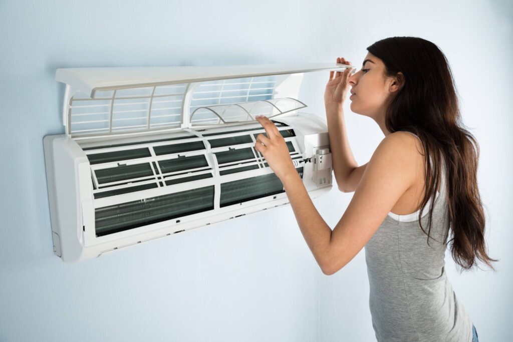 young woman checking air conditioner that's blowing hot air